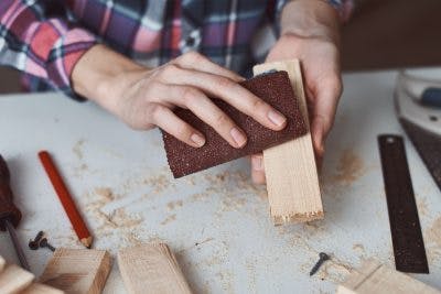 close up of woman's hands sanding piece of wood on workbench