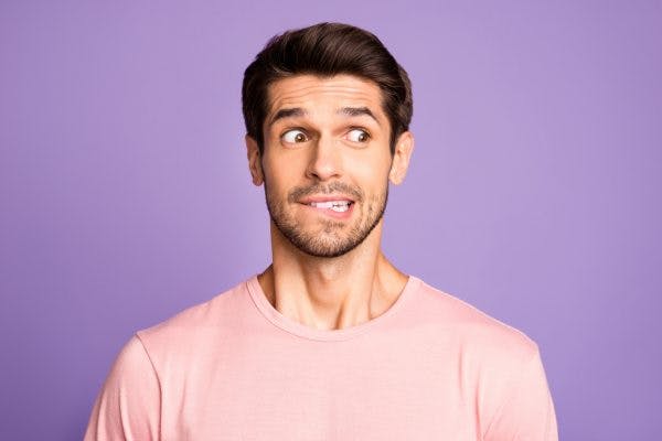 Close-up portrait of bearded guy wearing pink tshirt in front of isolated over violet purple lilac background biting lip looking nervous because he has damage to Wernicke's area