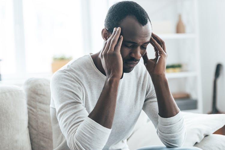 man sitting on couch rubbing head to help with his mild TBI recovery