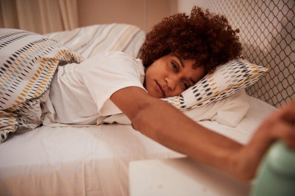 woman reaching for her alarm clock, struggling to wake up because she has post-traumatic hypersomnia