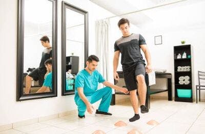 physical therapist in scrubs helping cerebellar stroke patient walk through balance exercise