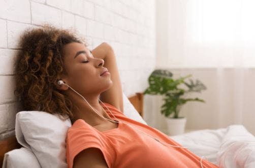 woman with headphones relaxing on bed listening to podcast