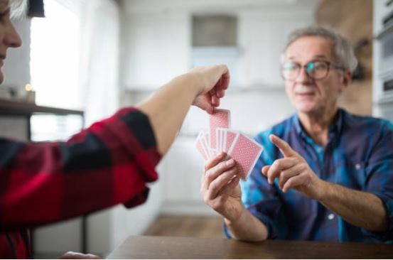 stroke patient holding playing cards while someone picks a random card from their hand