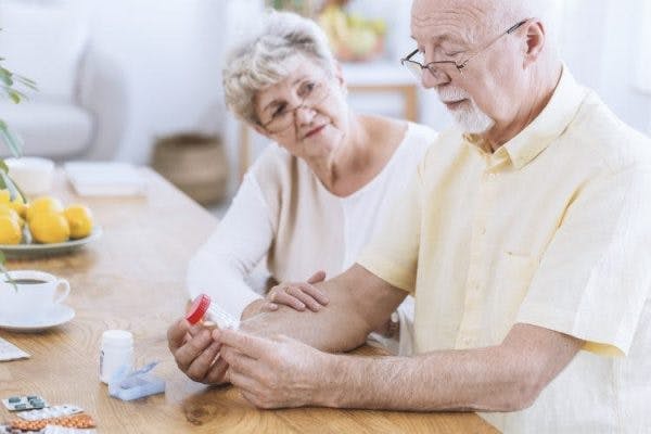stroke patient with reading glasses on looking at medication label with his caregiver