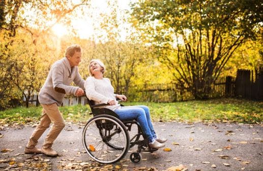 caregiver pushing stroke patient in wheelchair through path with colorful trees and falling leaves