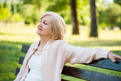 peaceful-looking stroke patient sitting on park bench with eyes closed visualizing herself recovering from stroke