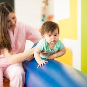 Therapist helping baby stroke survivor crawl on a balance beam