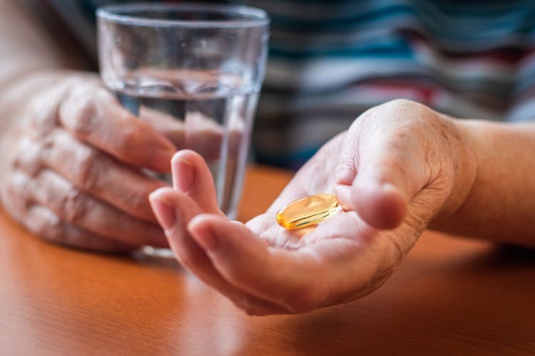 woman's hand holding fish oil tablets and glass of water