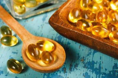 fish oil tablets on wooden spoons and wooden platter over blue table