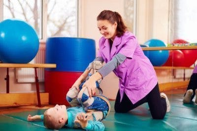 physical therapist stretching child's legs on exercise mat