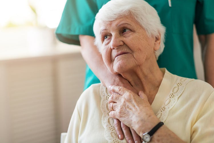 Close-up of elderly post-stroke dementia patient holding her caregiver's hand which is on her shoulder