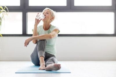 gesunder Schlaganfallpatient nippt an Wasser, während er zu Hause auf Yogamatte entspannt