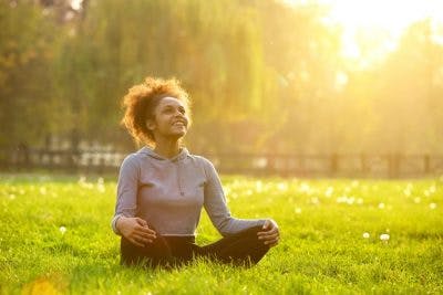 Woman sitting cross-legged on grass looking at the sky and smiling