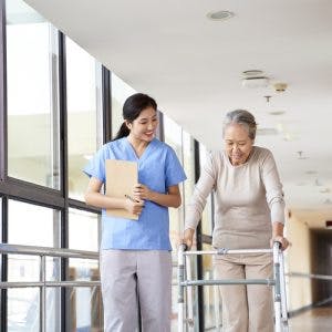 rehabilitation nurse standing next to stroke patient using a walker to recover from paralysis