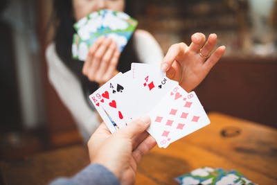 point of view shot of man holding playing cards in his hand while woman  is reaching across table and taking one of his cards