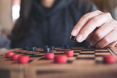 close-up of hand moving checkers piece, one of the best games for stroke patients