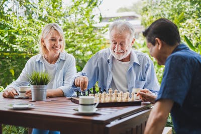 stroke patient playing chess game with his adult son on table outside while adult daughter watches 