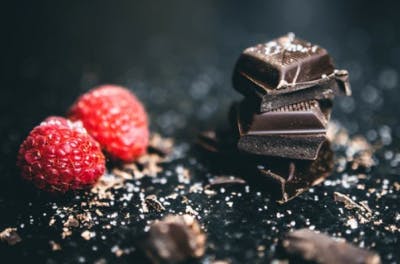 pieces of dark chocolate and raspberries on a black marble counter