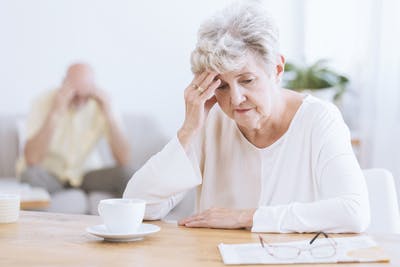 elderly woman sitting at kitchen table looking stressed because she has transcortical sensory aphasia