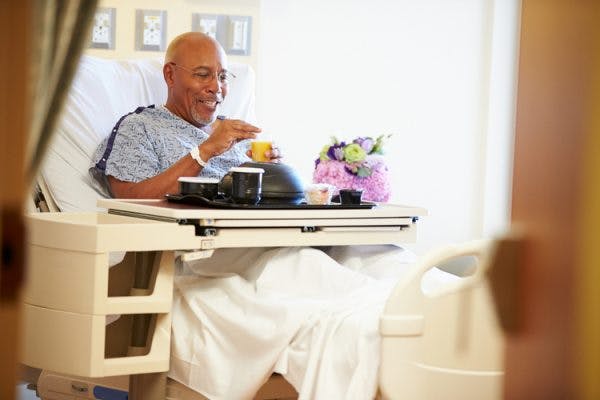 man in hospital bed with tray of food catered for dysphagia after brain injury
