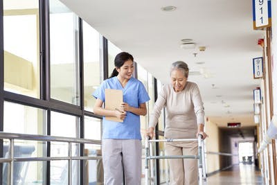 Une infirmière aide une patiente atteinte d'AVC à marcher dans le couloir en se servant d'une marchette.