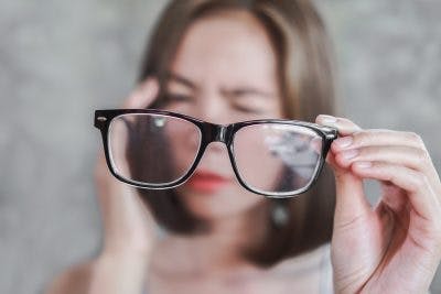 woman squinting and holding pair of glasses to represent vision problems that can impair driving after brain injury