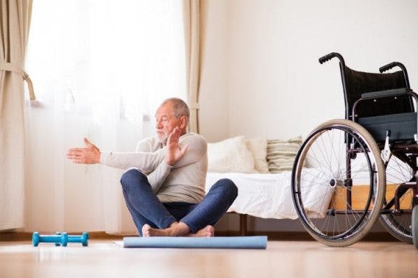 Adulto mayor paciente con accidente cerebrovascular sentado en un tapete de yoga haciendo estiramientos de fisioterapia con el brazo