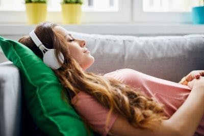 woman lying on couch closing her eyes while wearing headphones