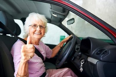 elderly woman giving thumbs up while in driver's seat of red car