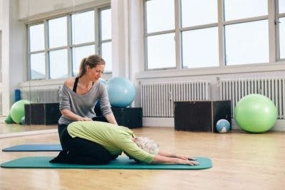 Une instructrice aide une patiente attente d'AVC à effectuer un exercice de yoga pour rétablir l'équilibre.