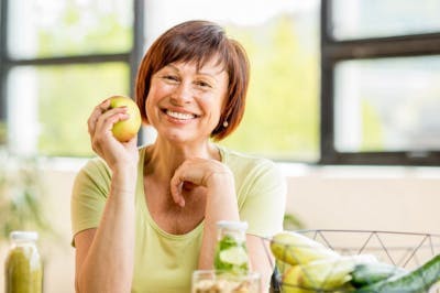 Une femme à pleine sourire vous offre une pomme de terre pour exemplifier le régime MIND qui aidera votre récupération après un AVC.