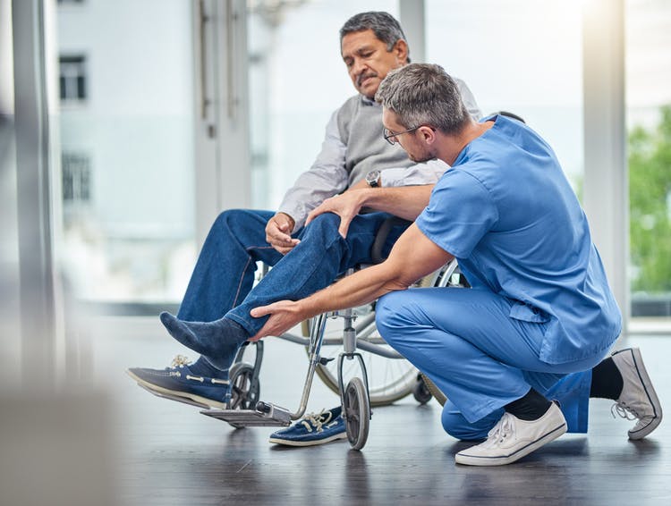 physiotherapist helping spinal cord injury patient adjust his legs to relieve pain