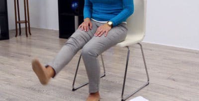 La physiothérapeute assise déplie sa jambe gauche en faisant l’exercice.    