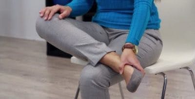 La physiothérapeute assise, les jambes croisées droite sur gauche, se pose pour vous montrer le commencement de l’exercice.  