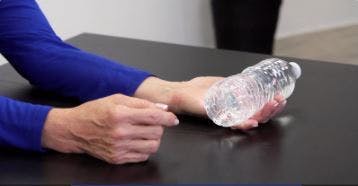 Le dos de la main affectée à table, portant une bouteille de l'eau, l'ergothérapeute vous montre le début de l'exercice.