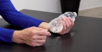 L'ergothérapeute fait enrouler les doigts autour de la bouteille pour effectuer l'exercice.