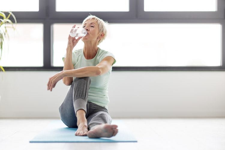 Une thérapeute avec l’air d’une instructrice de yoga fait une petite pause pour boire une bouteille de l’eau et vous accueillir aux exercices de rééducation après un AVC.