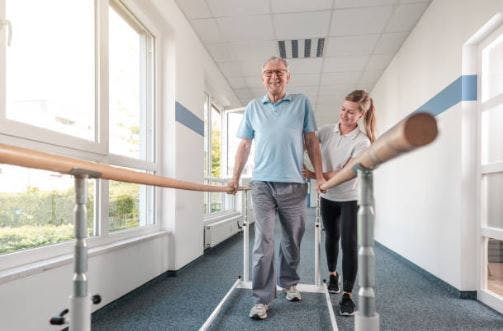 Patient d'AVC de sexe masculin utilisant des barres d'appui pour marcher pendant la séance de rééducation des patients hospitalisés