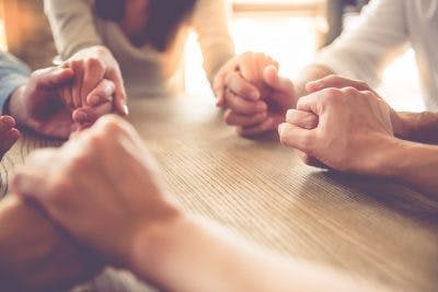 gros plan d'un groupe de personnes se tenant la main autour d'une table dans la lumière de l'après-midi