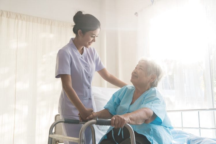 Une soignante aide une patiente à se lever de lit, se servant d'une marchette, pour commencer à profiter de la rééducation et se rétablir après un AVC.