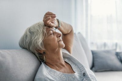 Une patiente très fatiguée, assise sur son canapé avec les yeux fermés, vous montre le principale symptôme du sommeil excessif après un AVC.