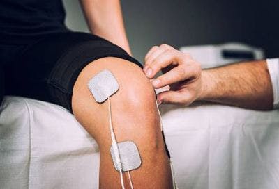 治疗师将电刺激垫应用于患者的膝盖以进行中风恢复