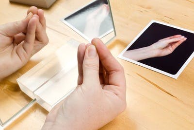 a hand in the position of a hand therapy exercise with a tabletop mirror showing a reflection of it