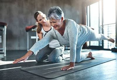 stroke survivor in clinic doing core exercises on mat with physiotherapist beside her