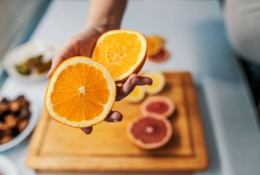 cutting board with citrus and someone holding two halves of an orange packed with vitamins for brain injury recovery