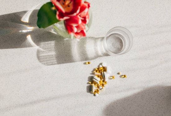 glass of water on a table next to a pile of a variety of vitamins for brain damage