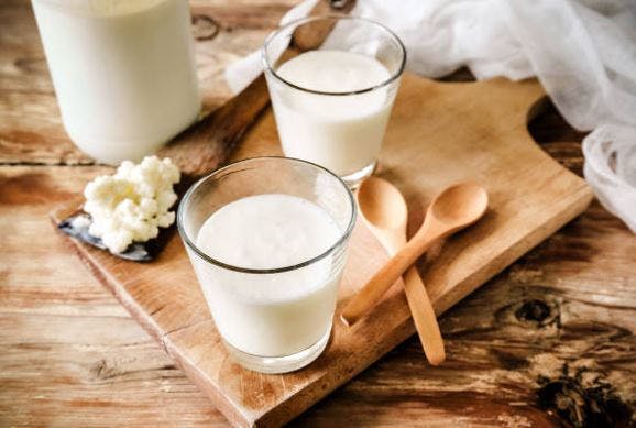 two cups of yogurt sitting on a wooden cutting board with eating spoons