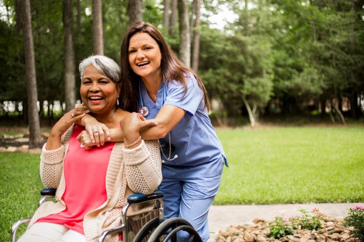 护理人员抱着轮椅上的妇女，在生命的各个阶段都表现出脑瘫的迹象和症状
