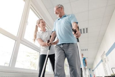 nurse helping a stroke survivor walk with two canes to prepare for leaving the hospital