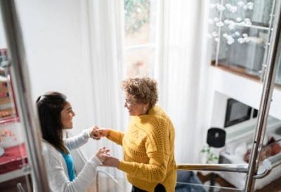 home nurse helping cerebellar brain injury survivor safely walk down stairs by guiding her and holding her hands